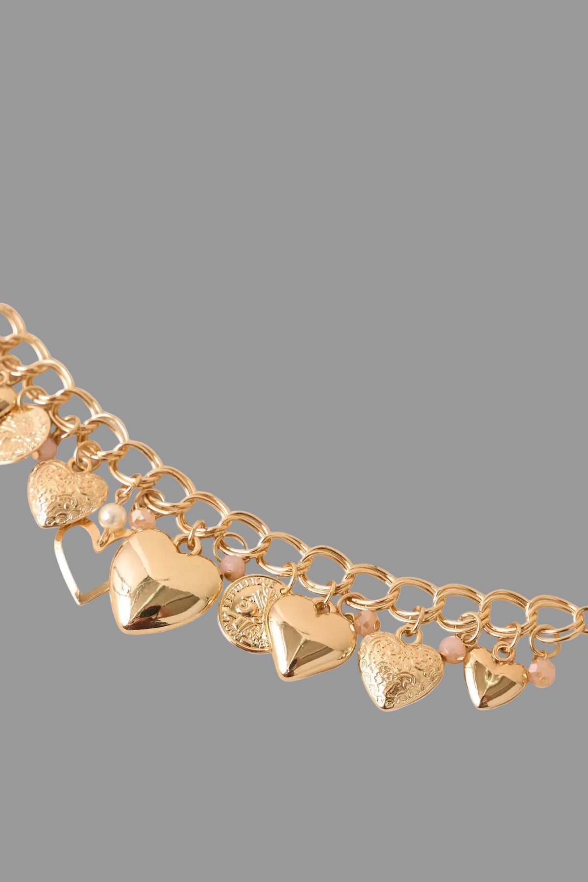 Gold tone charm bracelet designed with layered chain links, it features polished heart charms, vintage-inspired coin accents, faux pearls, and soft crystal details that catch the light beautifully.
