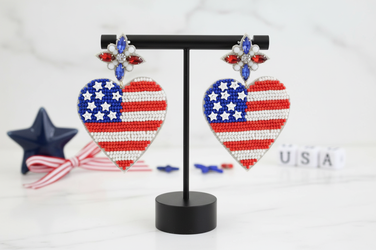 Red White Blue Seed Bead Heart Shaped Flag Earrings Patriotic Post Back Closure. Displayed on an earring display stand with red white blue banner in background and the letters U. S. A