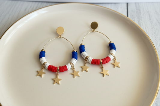 Pair of earrings with red, white, and blue disc beads on a beige plate.